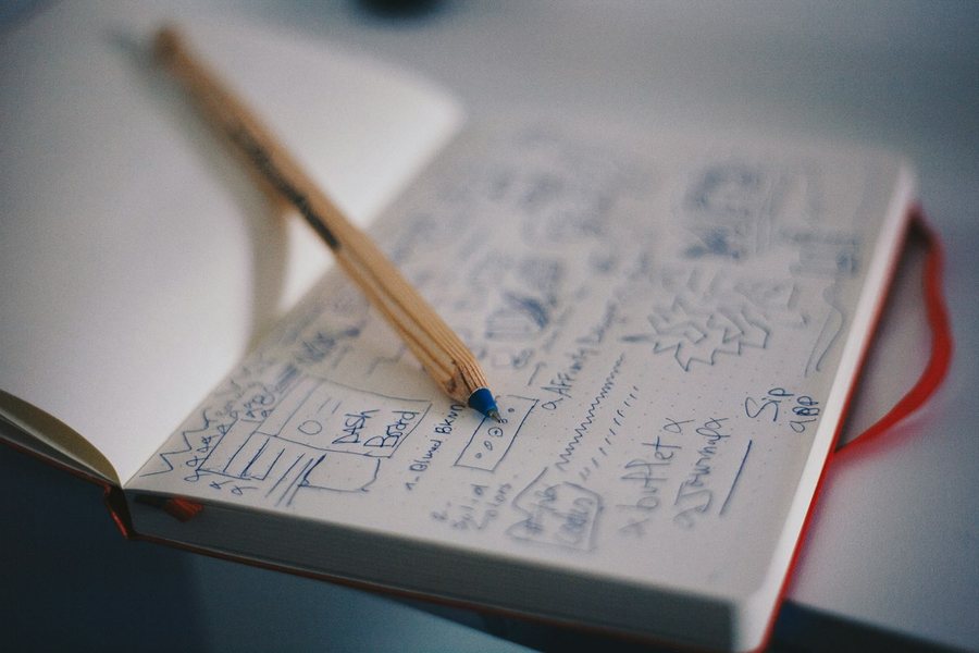 手書きの構想メモが広がるノートの上にペンが置かれている